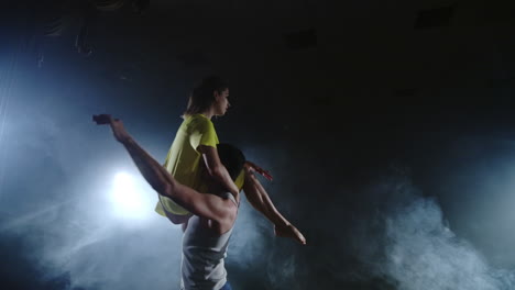 a-young-man-is-holding-a-woman-in-yellow-dress-holding-twirling-in-slow-motion-on-stage-in-smoke-and-spotlights